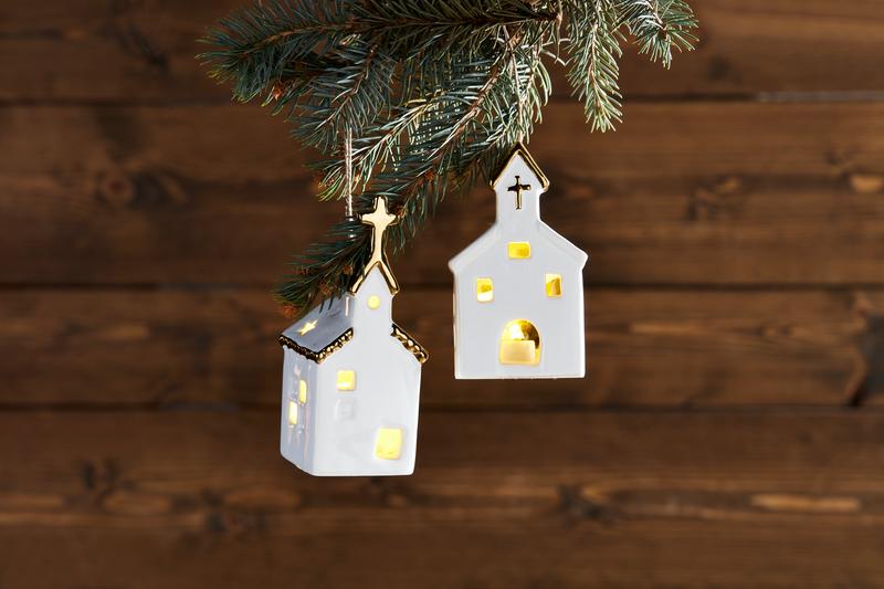 Decorative house-shaped lights hanging from a Christmas tree branch on a wooden background