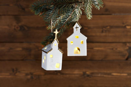 Decorative house-shaped lights hanging from a Christmas tree branch on a wooden background