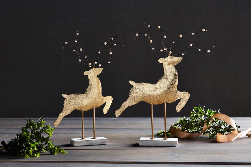 Two gold deer figurines on stands with a dark background